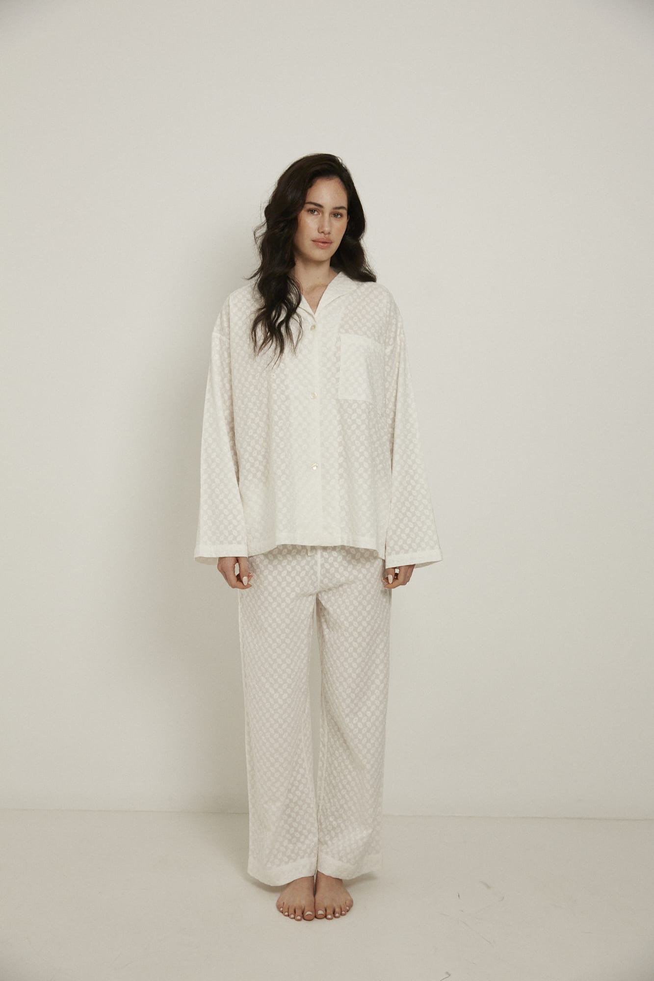 Women’s sleepwear set featuring an oversized, dropped-shoulder, button-through shirt, with natural shell buttons.  The loose-fit, straight-leg pants have an elasticated waist, flat front, and drawstring detail, and are comfortable and flattering. Made from white, 100% organic cotton, both pieces have been finished with French seams and feature delicate all-over embroidery.