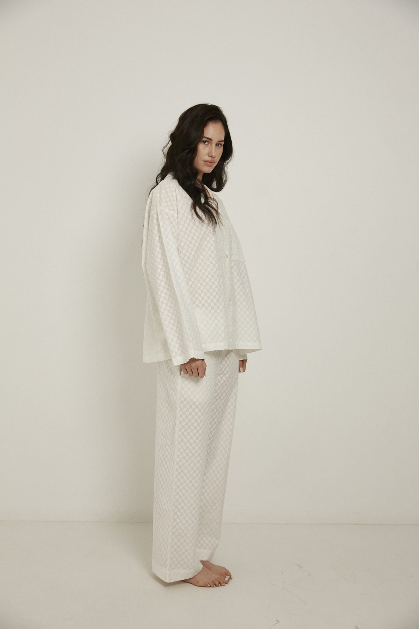 Women’s sleepwear set featuring an oversized, dropped-shoulder, button-through shirt, with natural shell buttons.  The loose-fit, straight-leg pants have an elasticated waist, flat front, and drawstring detail, and are comfortable and flattering. Made from white, 100% organic cotton, both pieces have been finished with French seams and feature delicate all-over embroidery.