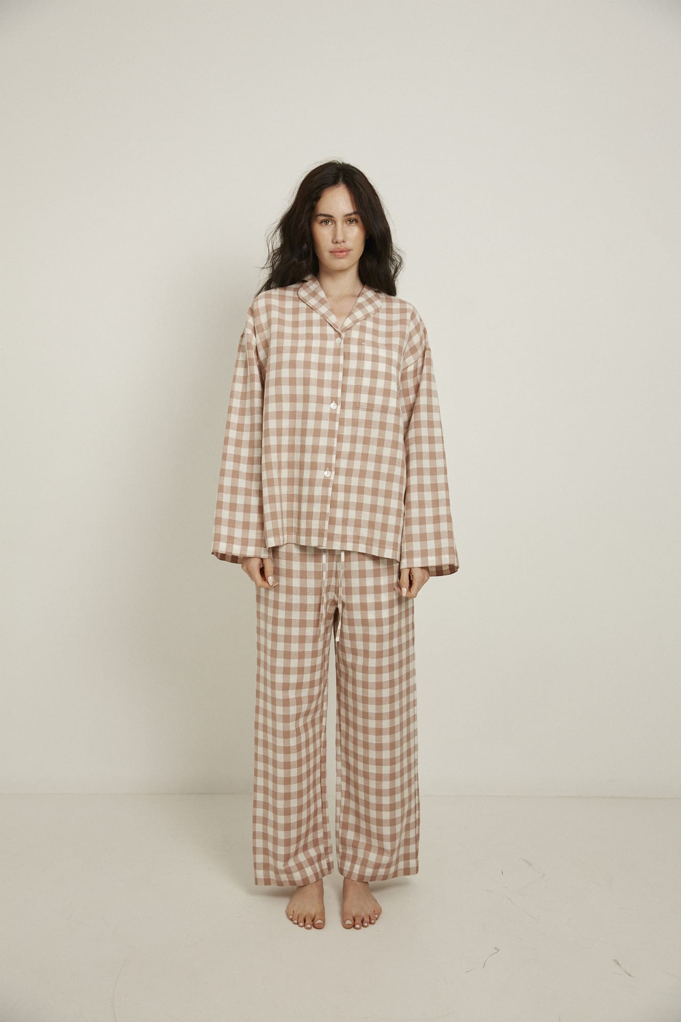 Women’s sleepwear set featuring an oversized, dropped-shoulder, button-through shirt, with natural shell buttons.  The loose-fit, straight-leg pants have an elasticated waist, flat front, and drawstring detail, and are comfortable and flattering. Made from an organic cotton and linen blend, in a pink and white check, both pieces have been finished with French seams.