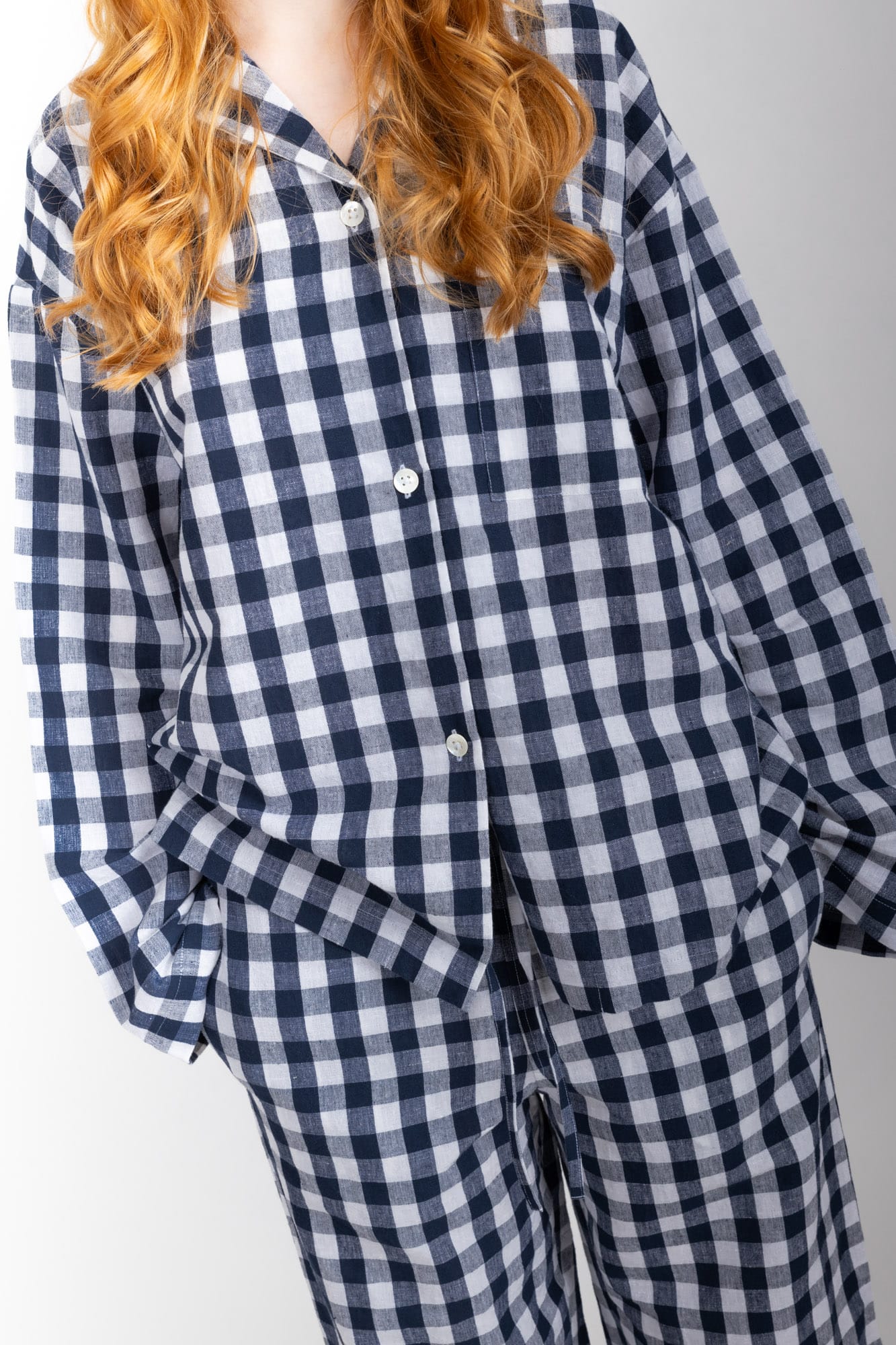 Women’s sleepwear set featuring an oversized, dropped-shoulder, button-through shirt, with natural shell buttons.  The loose-fit, straight-leg pants have an elasticated waist, flat front, and drawstring detail, and are comfortable and flattering. Made from an organic cotton and linen blend, in a navy and white check, both pieces have been finished with French seams.