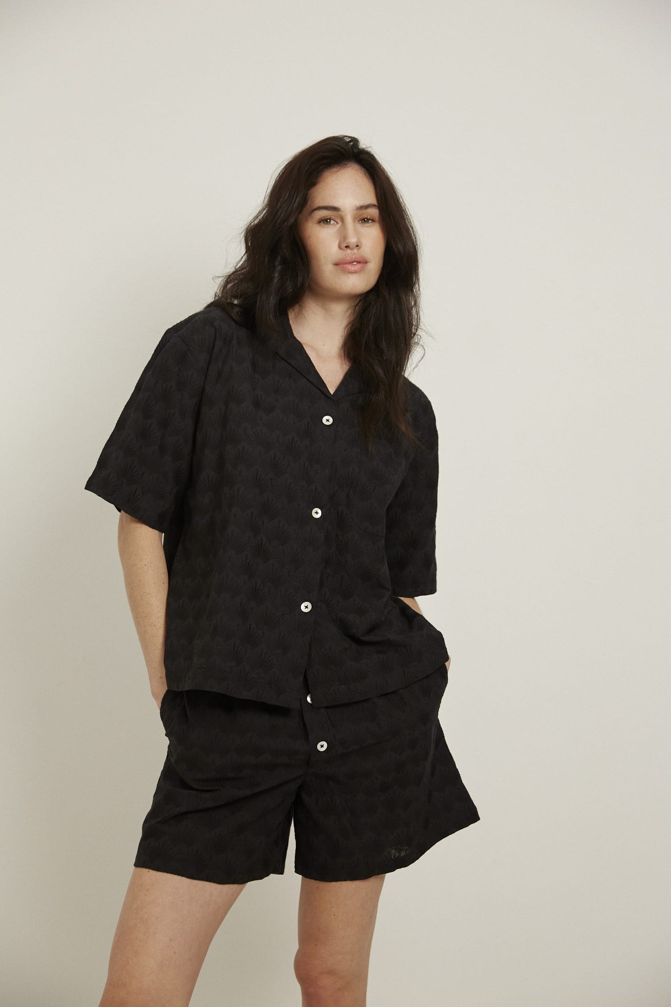 Women’s pyjama set including a short sleeve shirt and shorts. Made from 100% organic cotton, in black colour featuring delicate all over embroidery. The shirt has shell buttons, a front pocket and a back pleat with locker loop detail.  The shorts feature natural shell buttons and an elasticated waistband for comfort.