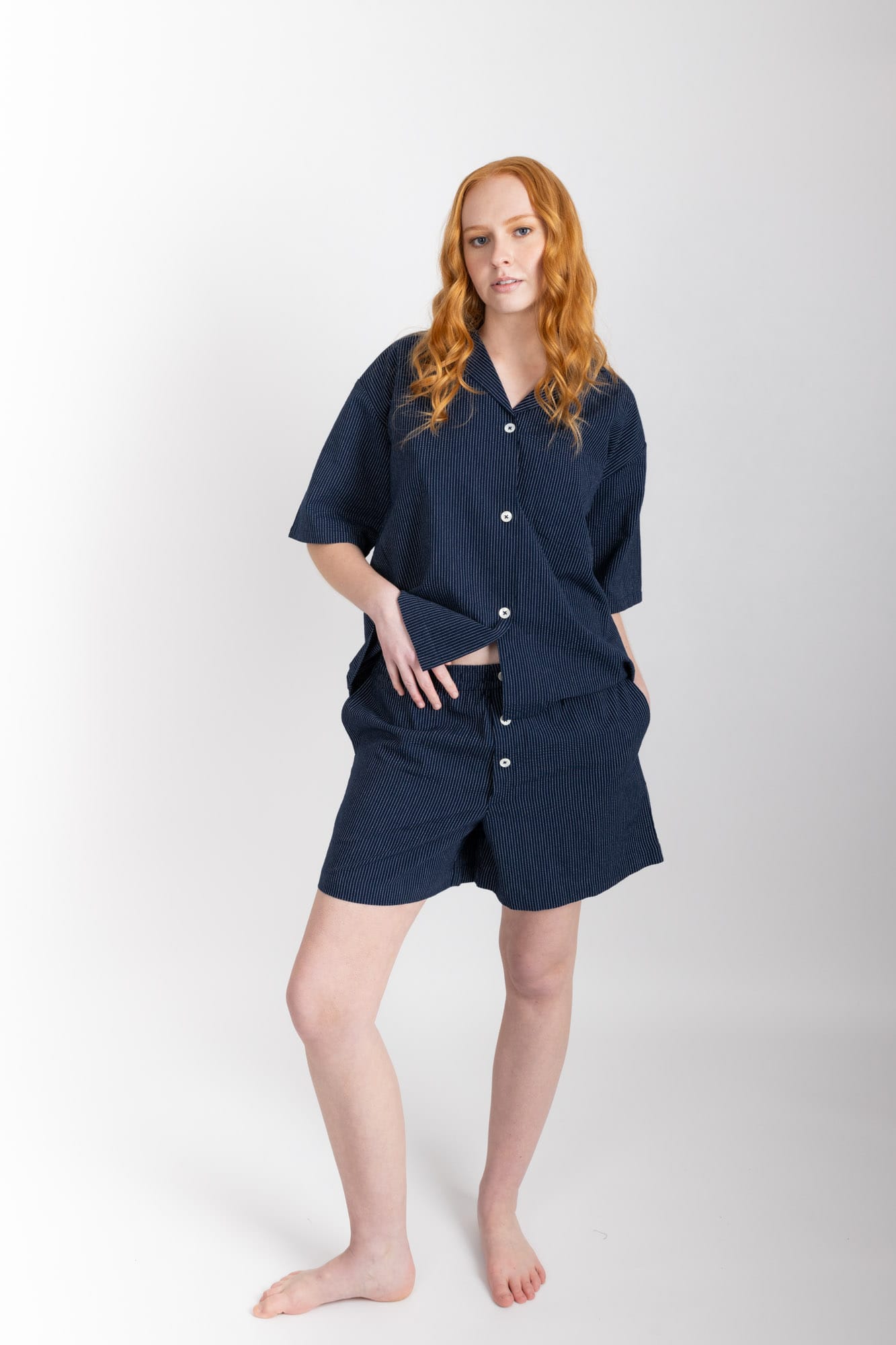Women’s pyjama set including a short sleeve shirt and shorts. Made from organic cotton, in Navy pinstripe.  The shirt has shell buttons, a front pocket and a back pleat with locker loop detail.  The shorts feature natural shell buttons and an elasticated waistband for comfort.