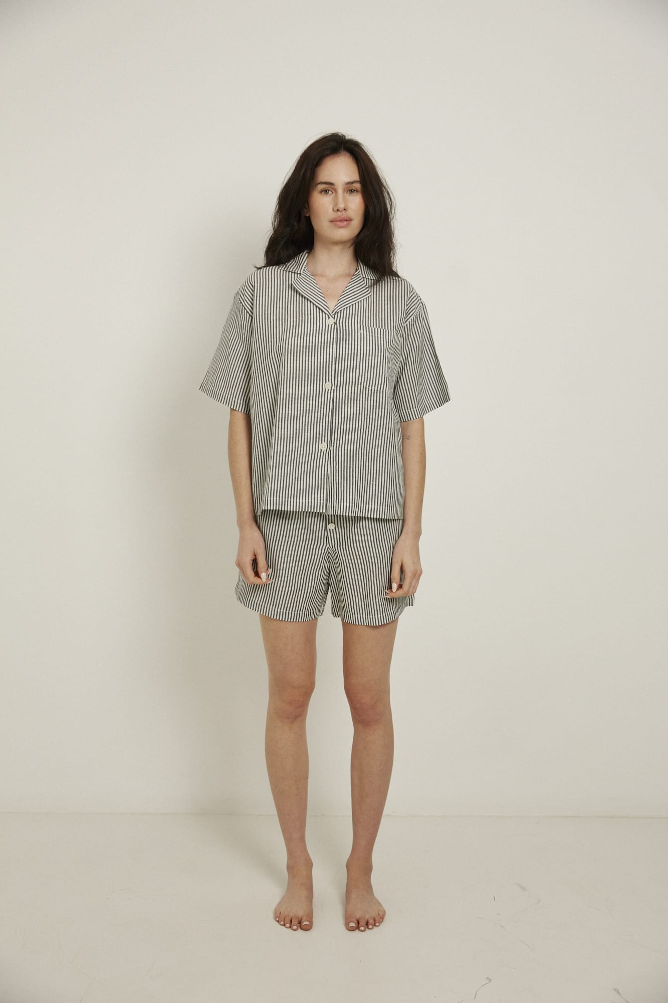Women’s pyjama set including a short sleeve shirt and shorts. Made from an organic cotton and linen blend, in a black and white stripe.  The shirt has shell buttons, a front pocket and a back pleat with locker loop detail.  The shorts feature natural shell buttons and an elasticated waistband for comfort.
