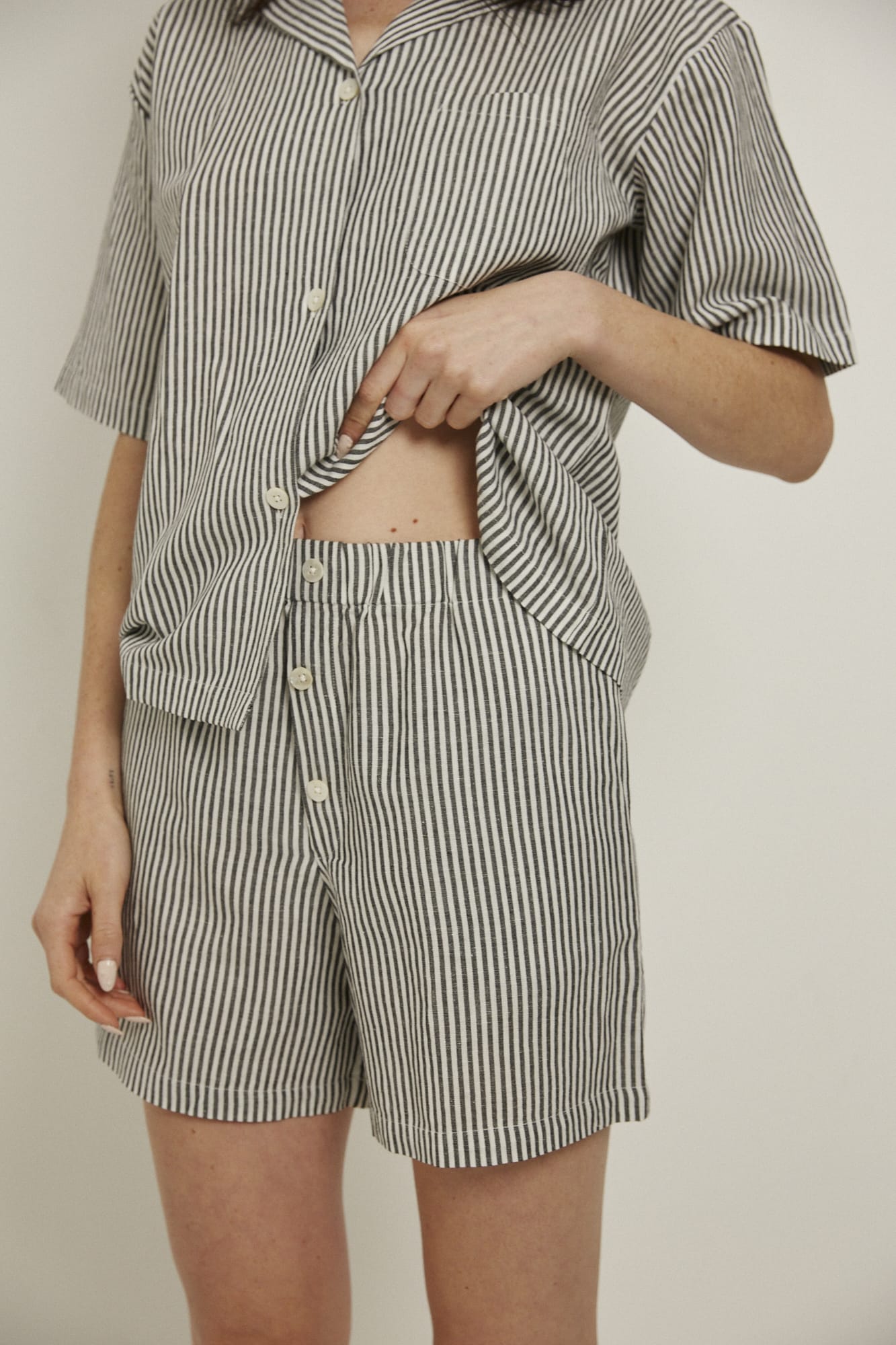 Women’s pyjama set including a short sleeve shirt and shorts. Made from an organic cotton and linen blend, in a black and white stripe.  The shirt has shell buttons, a front pocket and a back pleat with locker loop detail.  The shorts feature natural shell buttons and an elasticated waistband for comfort.