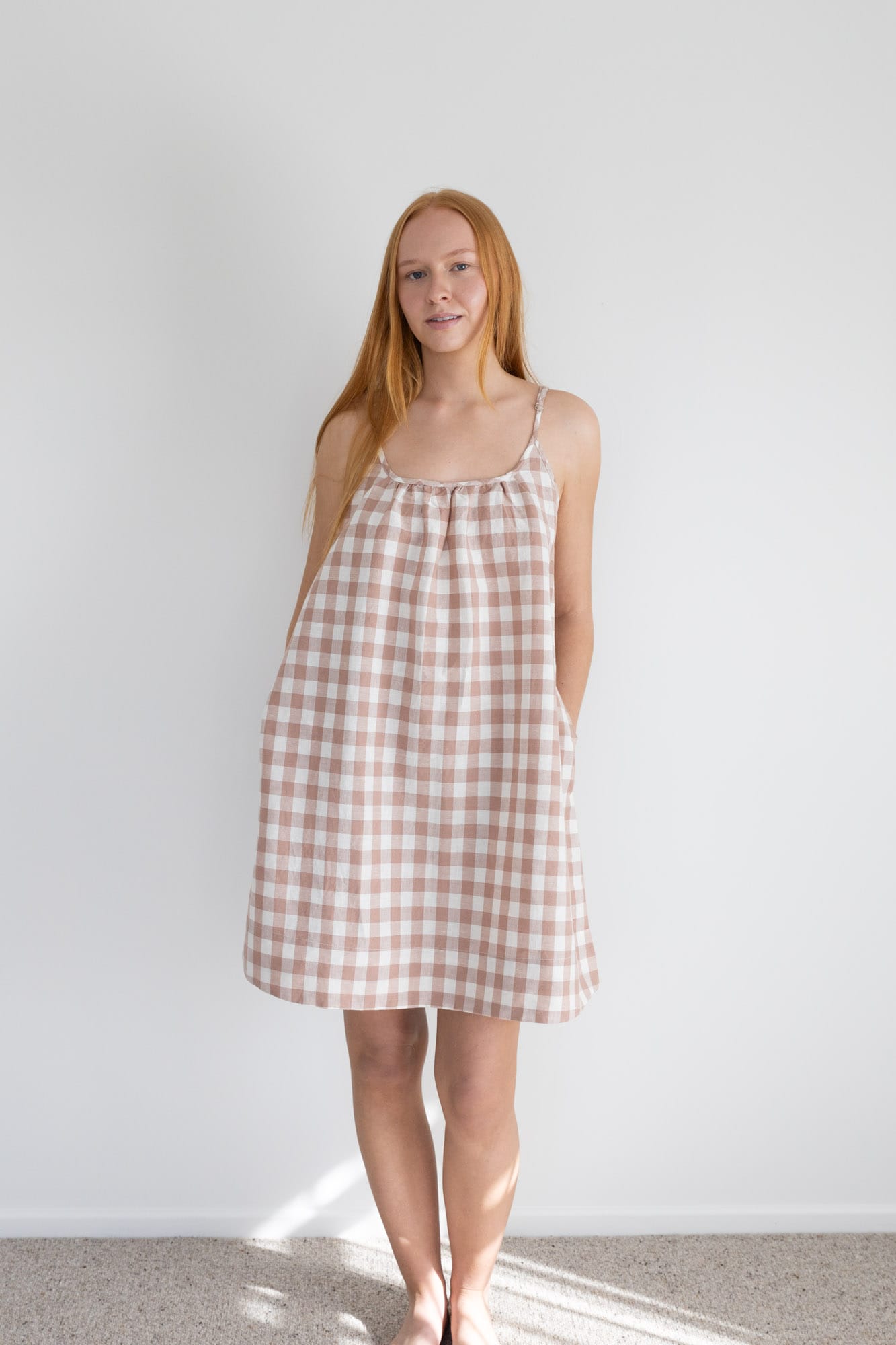 This knee length women’s nightdress dress features a scoop neck, adjustable spaghetti straps and side pockets. Finished with a wide hem, French seams, it is made from an organic cotton and linen blend, in a pink and white check