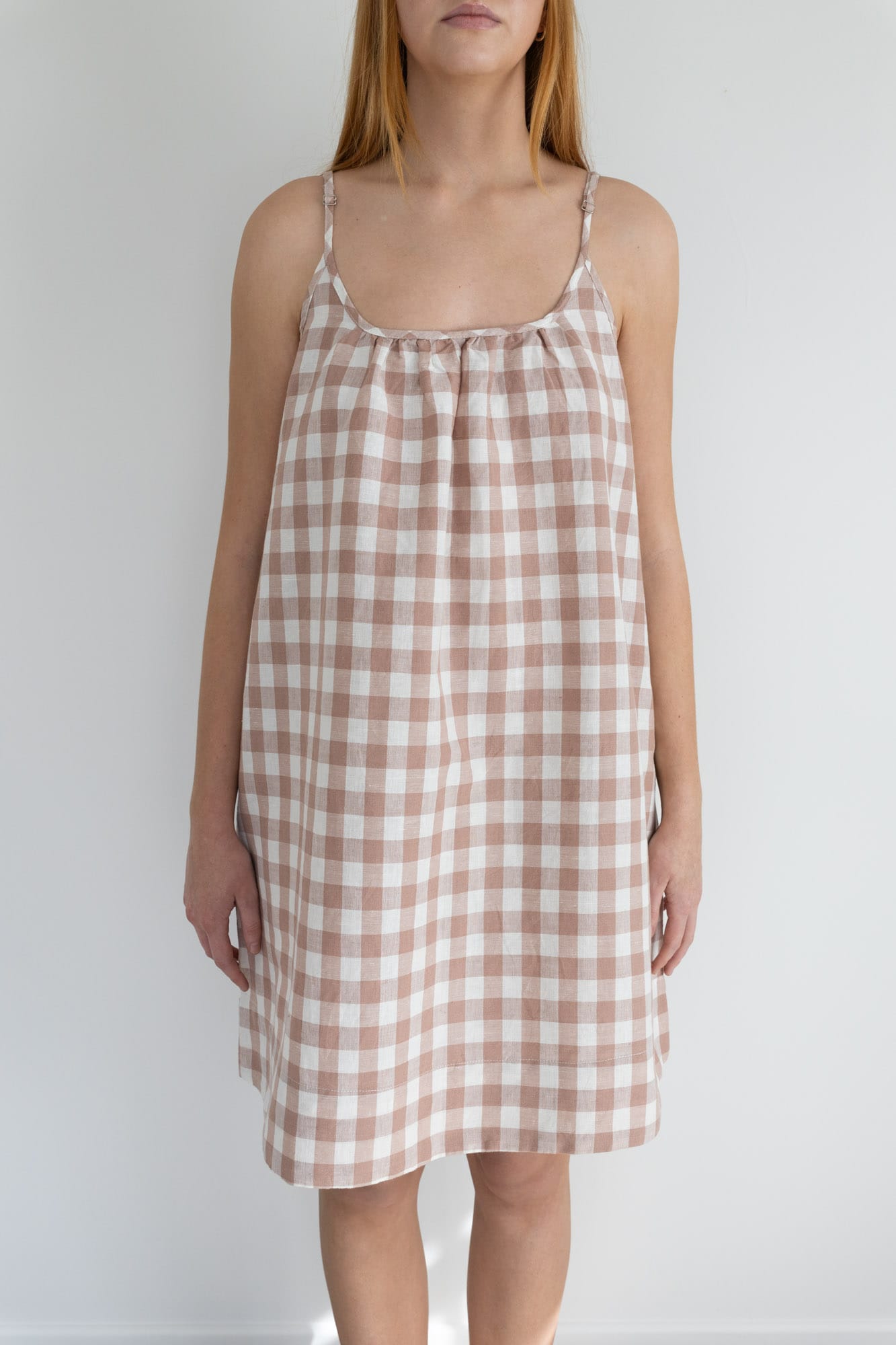 This knee length women’s nightdress dress features a scoop neck, adjustable spaghetti straps and side pockets. Finished with a wide hem, French seams, it is made from an organic cotton and linen blend, in a pink and white check