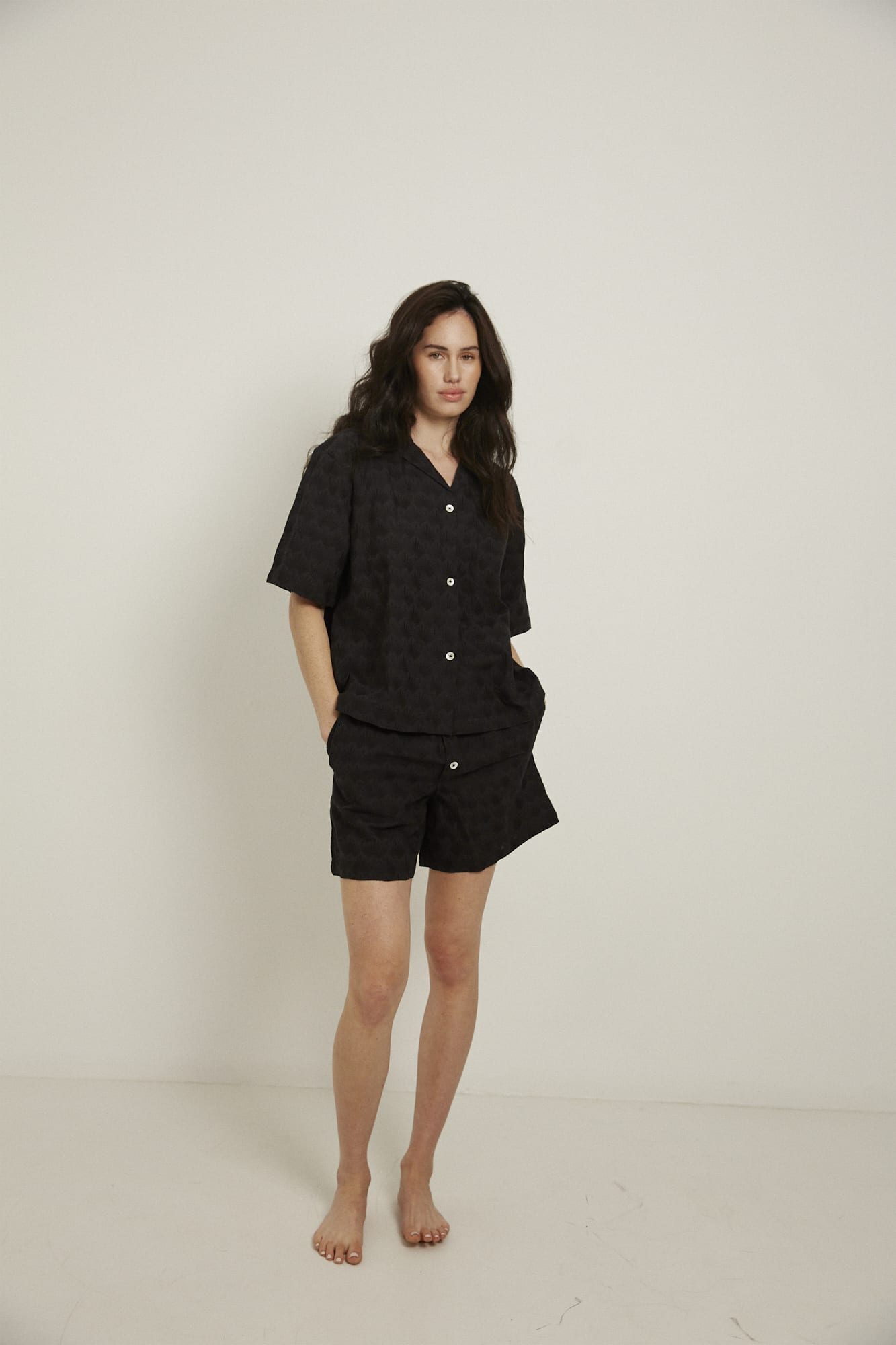 Women’s pyjama set including a short sleeve shirt and shorts. Made from 100% organic cotton, in black colour featuring delicate all over embroidery. The shirt has shell buttons, a front pocket and a back pleat with locker loop detail.  The shorts feature natural shell buttons and an elasticated waistband for comfort.